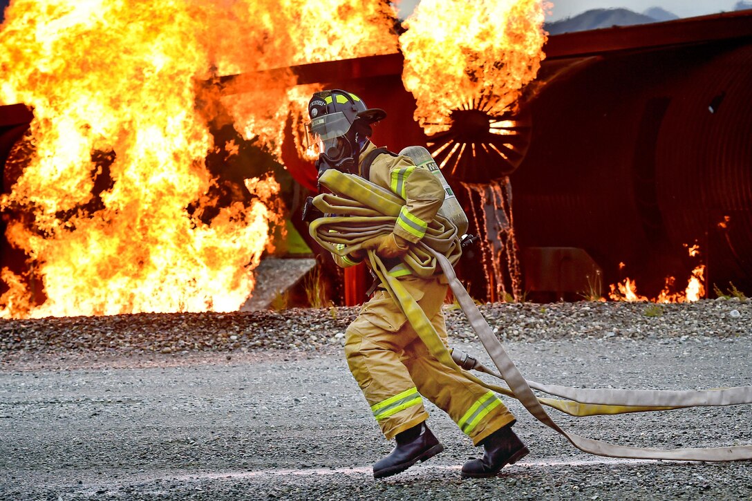An airman runs hose lines as an aircraft fire trainer burns in the background during firefighter training at Joint Base Elmendorf-Richardson, Alaska, Sept. 14, 2016. Air Force photo by Justin Connaher