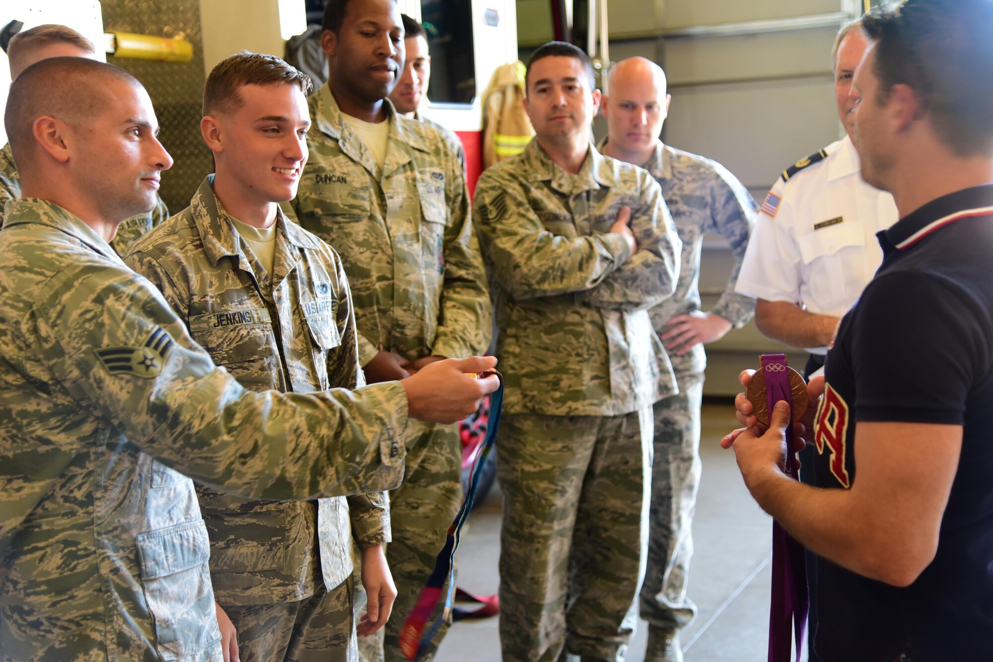 PETERSON AIR FORCE BASE, Colo. - Senior Airman Christopher Perry and Airman 1st Class Jacob Jenkins, 21st Civil Engineer Squadron firefighters, take turns holding an Olympic bronze medal provided by Troy Dumais, four-time U.S. Olympic diver, during the launch of the American300 group’s “Dive into Service” tour kicking off at Peterson Air Force Base, Colo., Sept. 12, 2016. Dive into Service is a mentor and relationship-building program that partners service members with U.S. Olympic Dive Team athletes to share like experiences as representatives of the United States. (U.S. Air Force photo by Staff Sgt. Amber Grimm)