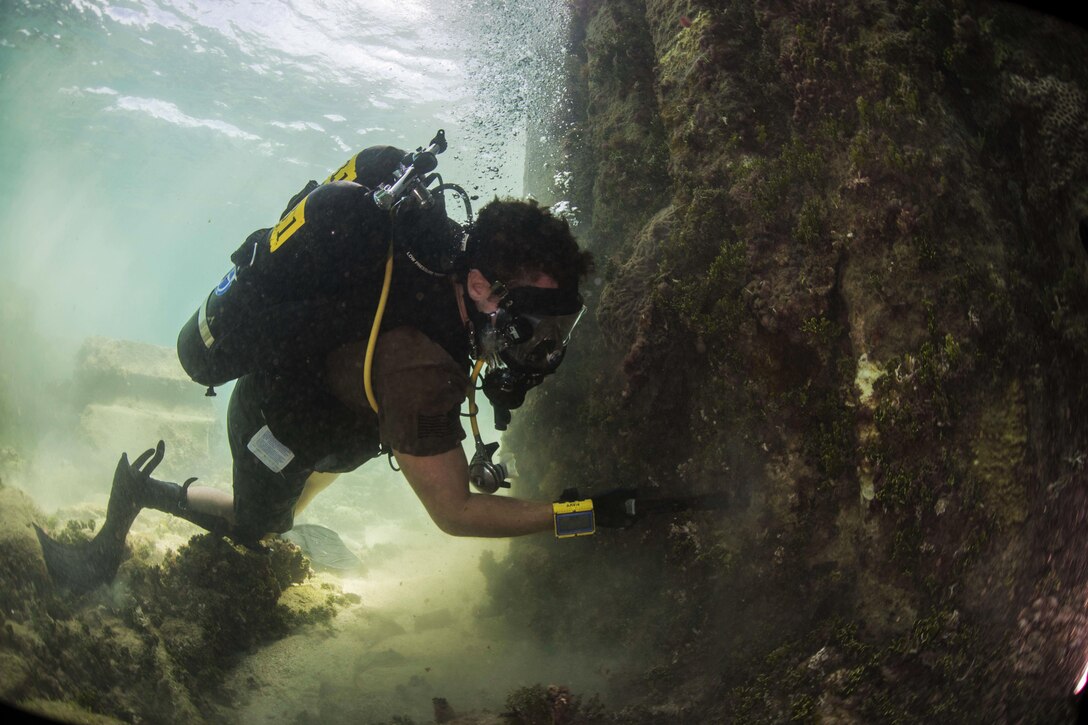 Navy Petty Officer 3rd Class Ryan Filo cleans growth from a pier while participating in Valiant Shield in Kwajalein, Marshal Islands, Sept. 15, 2016. The biennial exercise in and around Guam focuses on real-world proficiency in sustaining U.S. joint forces at sea, in the air, on land and in cyberspace. Navy photo by Petty Officer 2nd Class Daniel Rolston