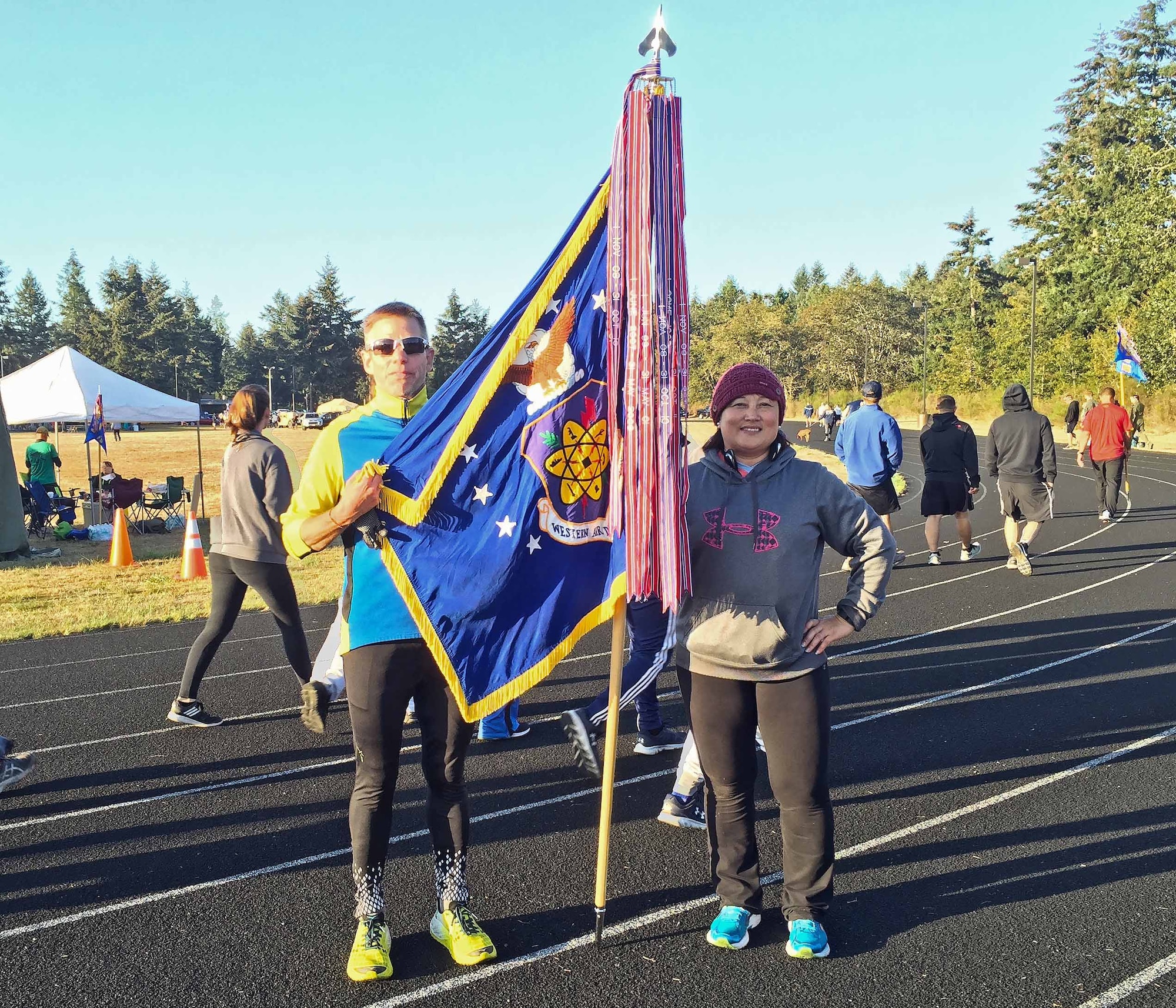Western Air Defense Sector team captains take a final lap with the unit flag around the track during the POW/MIA Remembrance 24 Hour Run on Joint Base Lewis-McChord Sept. 15.  Master Sgt. Diana Feeley, right, personally logged 24.5 miles and Bruce Robie, left, completed 41 miles during the 24-hour period.  Overall, the WADS team members logged 1,037 laps for a total of 259 miles to raise awareness of the U.S. military personnel taken as prisoners of war or listed as missing in action.  (Courtesy photo)