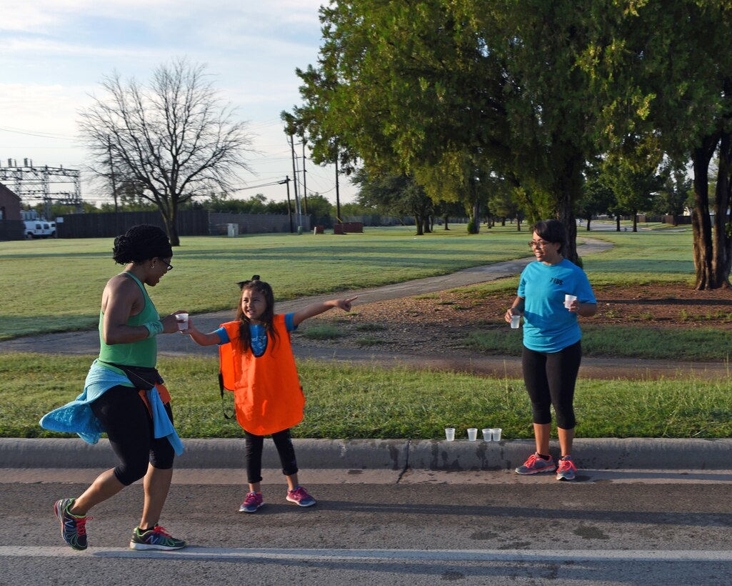 U.S. Air Force Staff Sgt. Marcela Huerta, 7th Force Support Squadron fitness assessment cell manager, watches as her daughter, Akira, gives water and directions to Mica Jones, personal trainer and fitness instructor, during the Dyess Mini Marathon at Dyess Air Force Base, Texas, Sept. 17, 2016. More than 15 volunteers were present at several checkpoints to assist over 50 participants by providing water and directions for each particular race route. (U.S. Air Force photo by Senior Airman Kedesha Pennant)