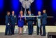 A cadet from Civil Air Patrol’s Middle East Region holds the Civil Air Patrol flag as Secretary of the Air Force Deborah James affixes a red, white and blue streamer signifying presentation of the Air Force Organizational Excellence Award to CAP for the period of Oct. 1, 2012-Aug. 31, 2016. Present for the ceremony were, from left, a second CAP cadet; Gen. David L. Goldfein, Air Force chief of staff; Maj. Gen. Joe Vazquez, CAP national commander; and Rick Broome, the noted aviation artist whose painting of a CAP intercept mission was presented to the Air Force for permanent display in the Pentagon. The presentation occurred at the Air Force Association’s Air, Space & Cyber Conference at the Gaylord National Resort and Convention Center in National Harbor, Maryland. (U.S. Air Force Photo)