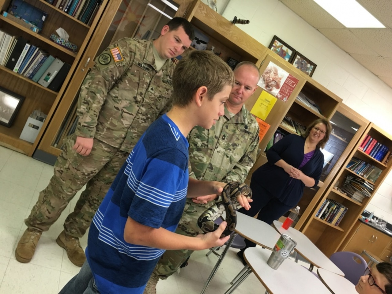 Eighth-grade Earth science student Blayne Smith does a show-and-tell of his ball python, Killer, as Army Sgt. Jacob D. Wilson, U.S. Army Operational Test Command's command group noncommissioned officer in charge, left, and Army Master Sgt. Earnest L. Vance, OTC's Test Technology Directorate NCOIC, listen to Smith's presentation as Monica L. Mitchell, 8th-grade Earth Science teacher, observes at right during an OTC Adopt-A-School visit to Florence Middle School, Texas, Sept. 9, 2016. Army photo by Michael Novogradac