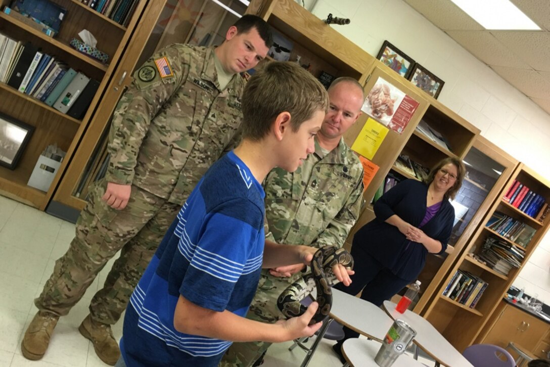 Eighth-grade Earth Science student Blayne Smith does a show-and-tell of his ball python, Killer, as Army Sgt. Jacob D. Wilson, U.S. Army Operational Test Command's command group noncommissioned officer in charge, left, and Army Master Sgt. Earnest L. Vance, OTC's Test Technology Directorate NCOIC, listen to Smith's presentation as Monica L. Mitchell, 8th-grade Earth Science teacher, observes at right during an OTC Adopt-A-School visit to Florence Middle School, Texas, Sept. 9, 2016. Army photo by Michael Novogradac