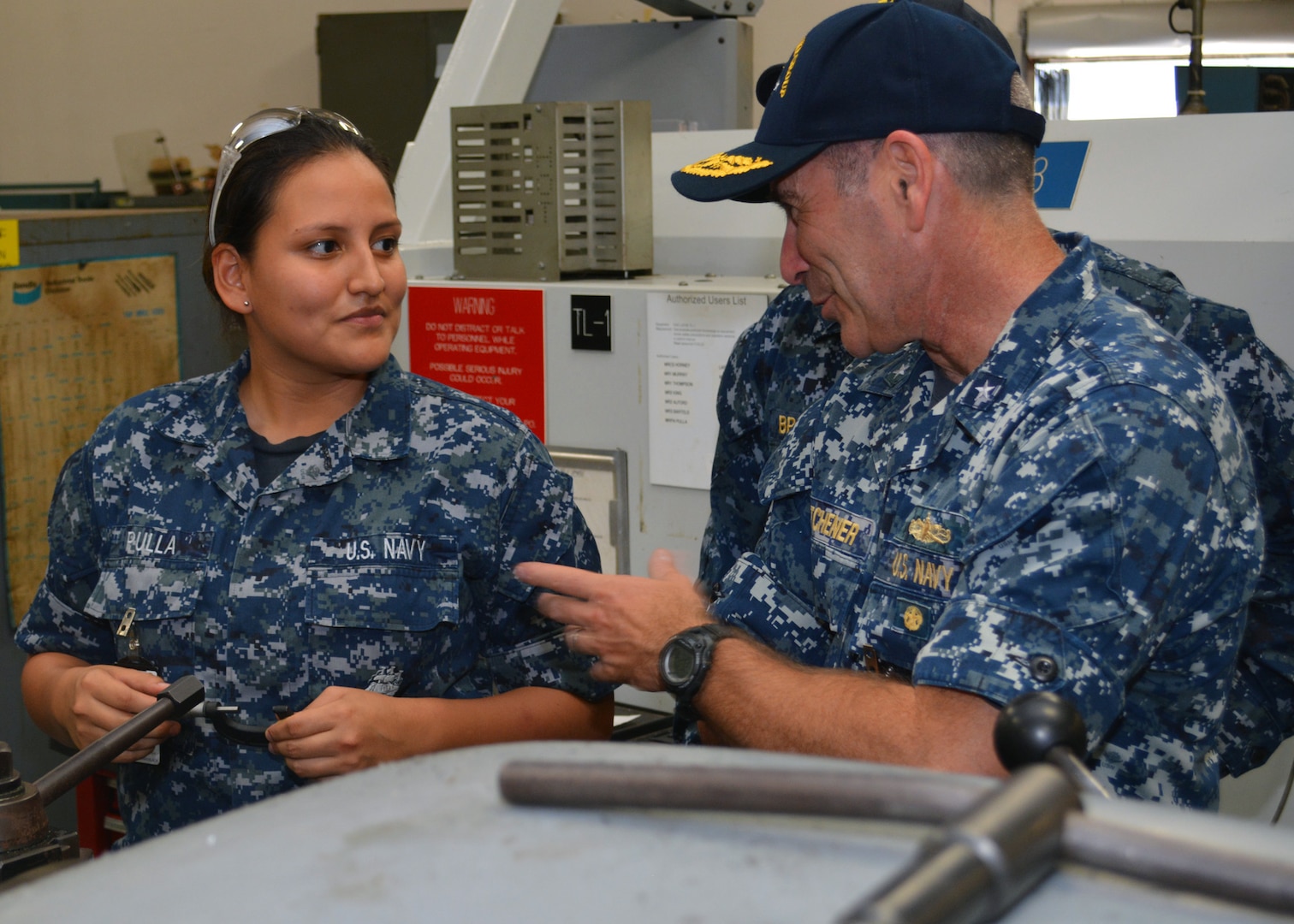 Machinery Repairman Fireman Jennifer Pulla demonstrates how she uses a lathe and specialized tools to manufacture replacement parts for ships home ported in Mayport, Fla., to Rear Adm. Roy Kitchener, Commander, Expeditionary Strike Group 2 at Southeast Regional Maintenance Center (SERMC) on Tuesday. Sailors attached to SERMC manufacture shaft sleeves, shafts, gears and other components for ships home ported in Mayport and operating within the 4th Fleet Area of Responsibility. 