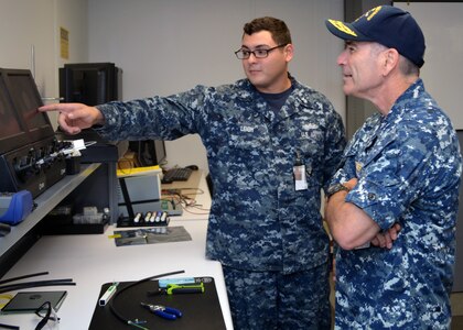 Fire Controllman 1st Class Andrew Leigh demonstrates to Rear Adm. Roy Kitchener, Commander Expeditionary Strike Group 2, how Sailors at Southeast Regional Maintenance Center (SERMC) test, clean and repair fiber optic cable. The 2M (Miniature/Micro-miniature) shop at SERMC can inspect, repair, fabricate and troubleshoot fiber optic cable onboard all applicable classes of U.S. Navy surface ships.