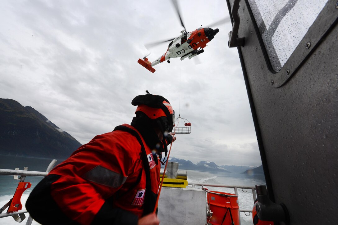 A Coast Guardsman tends the line of a hoist basket lowered by the aircrew of an MH-60 Jayhawk helicopter onboard the response boat-medium during rescue hoist training in Port Valdez, Alaska, Sept. 14, 2016. The helicopter crew is assigned to Coast Guard Forward Operating Location Cordova. Coast Guard photo by Petty Officer 1st Class Bill Colclough