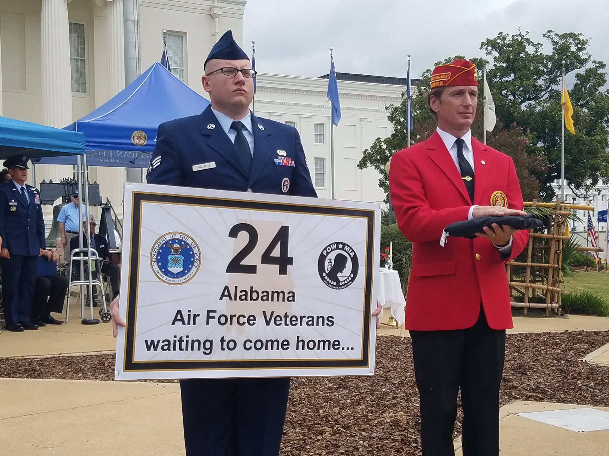 Senior Airman Brett Walters, Air Force Life Cycle Management Center, holds a sign indicating the number of Alabamians from the Air Force who are still in MIA status. During the ceremony, Brooks Barrow, Marine Corps league, escorted the American flag to each service representative while their service song played. (U.S. Air Force photo/Eric Sharman)