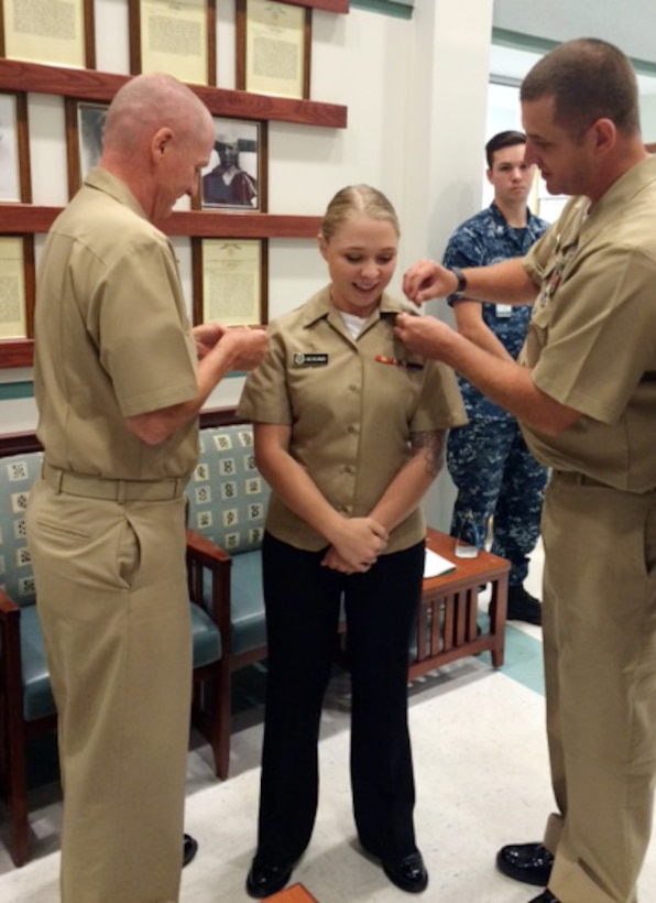 Capt. David Collins (left), commanding officer, Naval Hospital Jacksonville, Florida, and Chief Petty Officer Eric Jackson (right) Naval Branch Health Clinic-Albany, recently, pin new rank on the clinic’s first meritorious sailor, Petty Officer 3rd Class Hailey McAdams (center), laboratory assistant. McAdams’ fellow sailors and clinic personnel looked on during the historical ceremony, which was held at NBHC-Albany.
