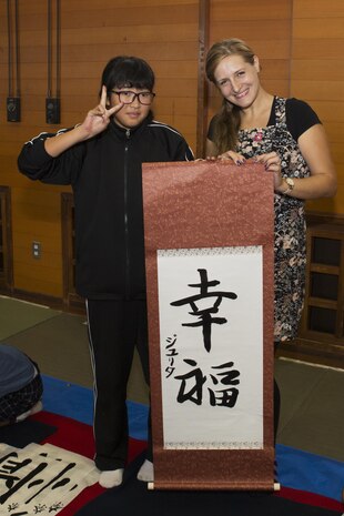 Julita Bryant, a Marine Corps Air Station Iwakuni resident, poses for a photo with calligraphy she painted at the Kumano Brush Festival in Kumano, Japan, Sept. 22, 2016. Air station residents traveled to Kumano with the Cultural Adaptation Program and were able to participate in a calligraphy competition with the Japanese locals. After attending the festival the residents visited the Fudenosato Kobo Museum where they learned how calligraphy equipment is made. (U.S. Marine Corps photo by Lance Cpl. Joseph Abrego)