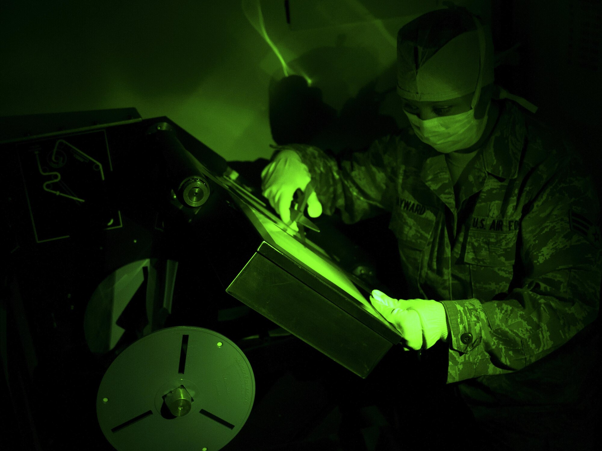 Senior Airman Heather Hayward, 9IS aerial film production specialist, cuts processed film during an Optical Bar Camera mission Feb. 17, 2015, at Beale Air Force Base, California. OBC Airmen work in a debris-free environment to develop 10,500 feet of film per mission, in either faint green light or complete darkness, using a Versamat 1140 film processor. From start to finish, it takes about nine hours to develop the entire film roll. (Air Force photo by Airman 1st Class Taylor A. Workman)