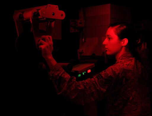 Senior Airman Shana Wojcik, the 9th Intelligence Squadron quality assurance section lead, threads the original negative film through a Niagara printer in preparation for creating a duplicate positive copy Sept. 9, 2016, at Beale Air Force Base, Calif. The printing process is essential to the Optical Bar Camera mission because it is the only version of the film that geospatial analysts can exploit. In this section, it is safe to work under red or yellow light to prevent light damage to the duplicate film. (U.S. Air Force photo/Airman 1st Class Taylor A. Workman) 