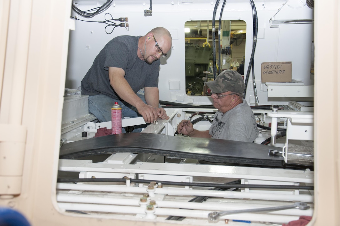 (Left) Kenneth Throenle and James Jacks, both heavy mobile equipment mechanics, work in the interior hull of a Hercules at Production Plant Barstow, Marine Depot Maintenance Command, to install hydraulic hoses that are the “arteries and veins” of the massive towing machine.