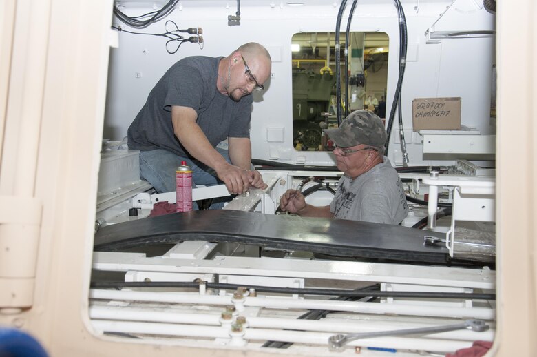 (Left) Kenneth Throenle and James Jacks, both heavy mobile equipment mechanics, work in the interior hull of a Hercules at Production Plant Barstow, Marine Depot Maintenance Command, to install hydraulic hoses that are the “arteries and veins” of the massive towing machine.