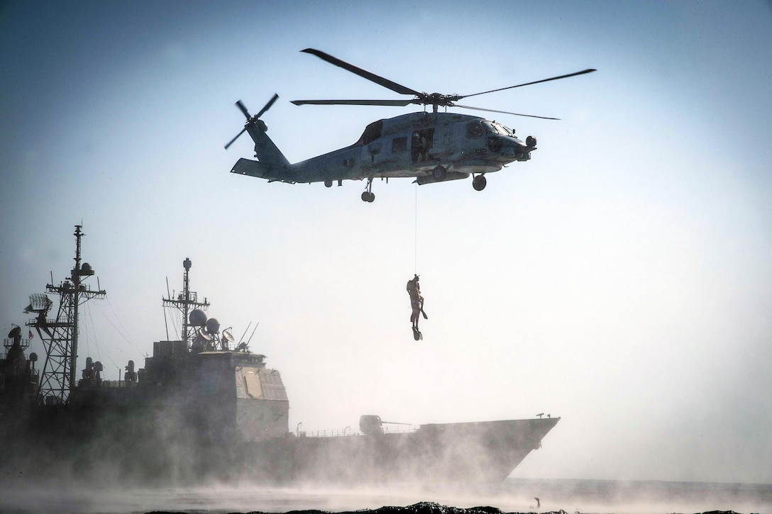 An MH-60R Seahawk helicopter hoists two sailors during search and rescue training in front of the USS Monterey in the Persian Gulf, Sept. 23, 2016. The Monterey is supporting maritime security operations and theater security cooperation efforts in the U.S. 5th Fleet area of operations. Navy photo by Petty Officer 2nd Class William Jenkins