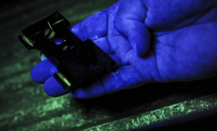John Sanders, M1 non-destructive inspection shop lead, demonstrates how the florescent magnetic particle inspection finds cracks in parts in the NDI lab on Nellis Air Force Base, Nev., Sept. 28. With these processes the NDI Lab can inspect each piece individually for cracks, breaks, or defects that the human eye can't see. (U.S. Air Force photo by Airman 1st Class Kevin Tanenbaum/Released)