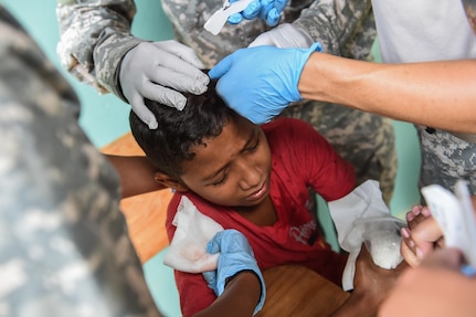 Members of the Joint Task Force-Bravo Medical Element team place two staples in the head of a young boy to stop the bleeding during a medical readiness training exercise, or MEDRETE, in the village of Bacadilla, Olancho district, Honduras, Sept. 22, 2016. MEDEL medics were able to quickly treat the boy who was playing outside the MEDRETE site and tripped while jumping across a ditch, striking his head on a sharp rock.