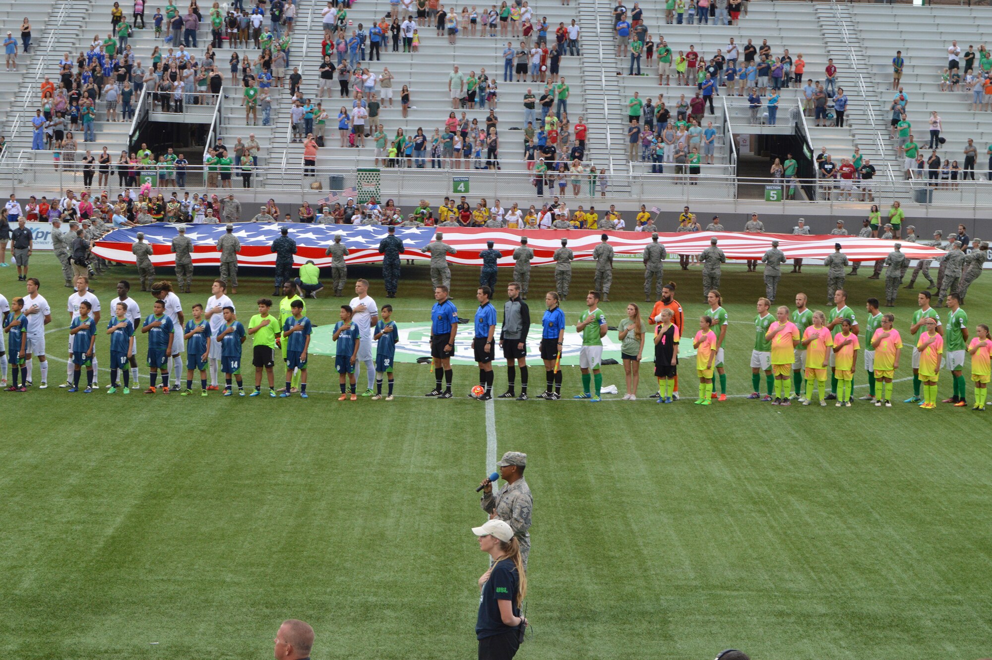 With volunteers from Tinker Air Force Base holding the giant American flag and the Oklahoma City Energy players behind him, Master Sgt. Robert Alford II sings the national anthem to open Military Appreciation Night Sept. 24. Sergeant Alford is the assistant superintendent for Logistics Readiness with the 552nd Maintenance Group. (Air Force photo by April McDonald)