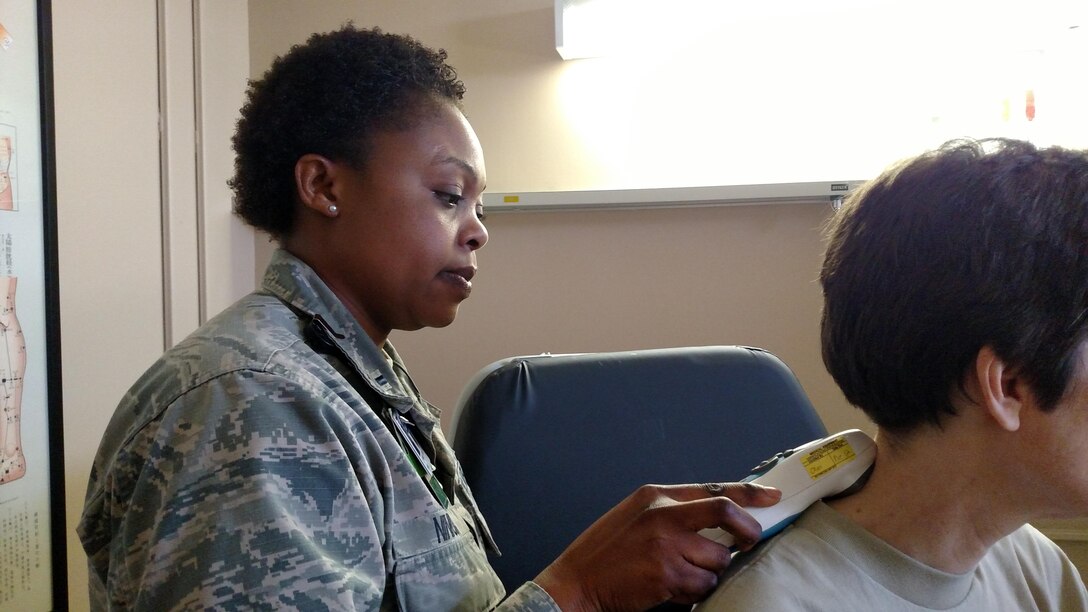 Lt. Folake Ninioloa, 779th Medical Group, Acupuncture and Integrative Medicine Center registered nurse applies a hand-held device to a patient to help relieve pain. The device delivers stimulation to nerves through the form of interactive electrical waves to reduce pain caused by injury and  inflammation. (Photo by Kathleen Tyler, 779 MDG)