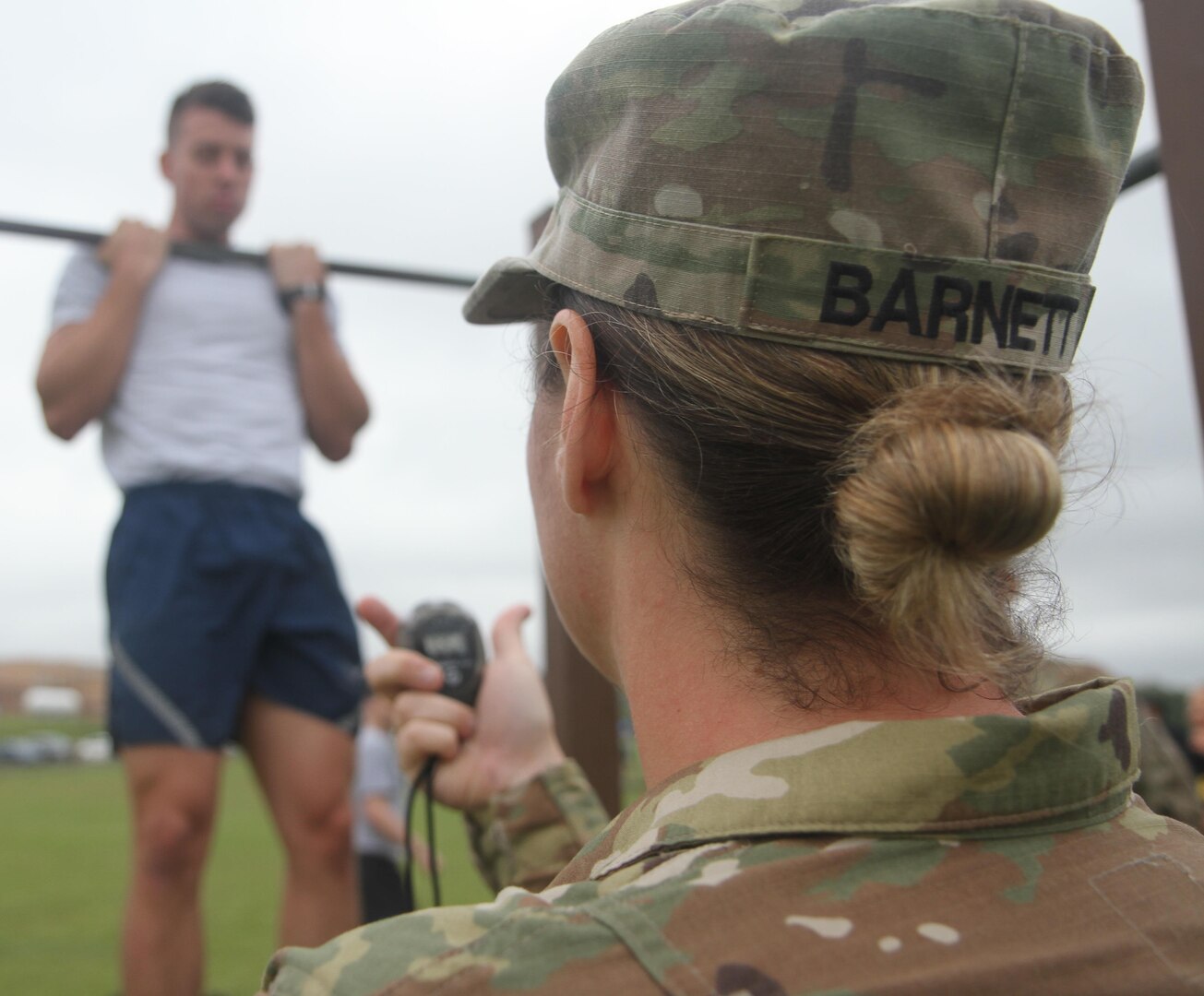 Army Staff Sgt. Cassie Barnett times an airmen completing the flexed-arm hang during day two of the German Armed Forces Proficiency Badge testing at Joint Base San Antonio-Camp Bullis April 1. The flexed-arm hang is one of three events service members completed during the military fitness portion of the GAFPB testing. 