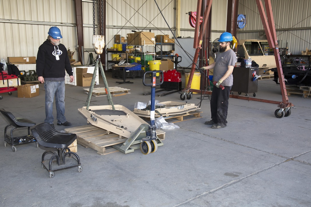 (Left) Rob Stickley and Steven Barela, both Heavy Mobile Equipment Mechanics, use a CATIII portable crane to life a heavy armored door that goes to a Logistics Vehicle System Replacement truck, March 9. The CATIII is just one innovation implemented by the Safety Office at Production Plant Barstow, Marine Depot Maintenance Command, aboard the Yermo Annex of Marine Corps Logistics Base Barstow, Calif.