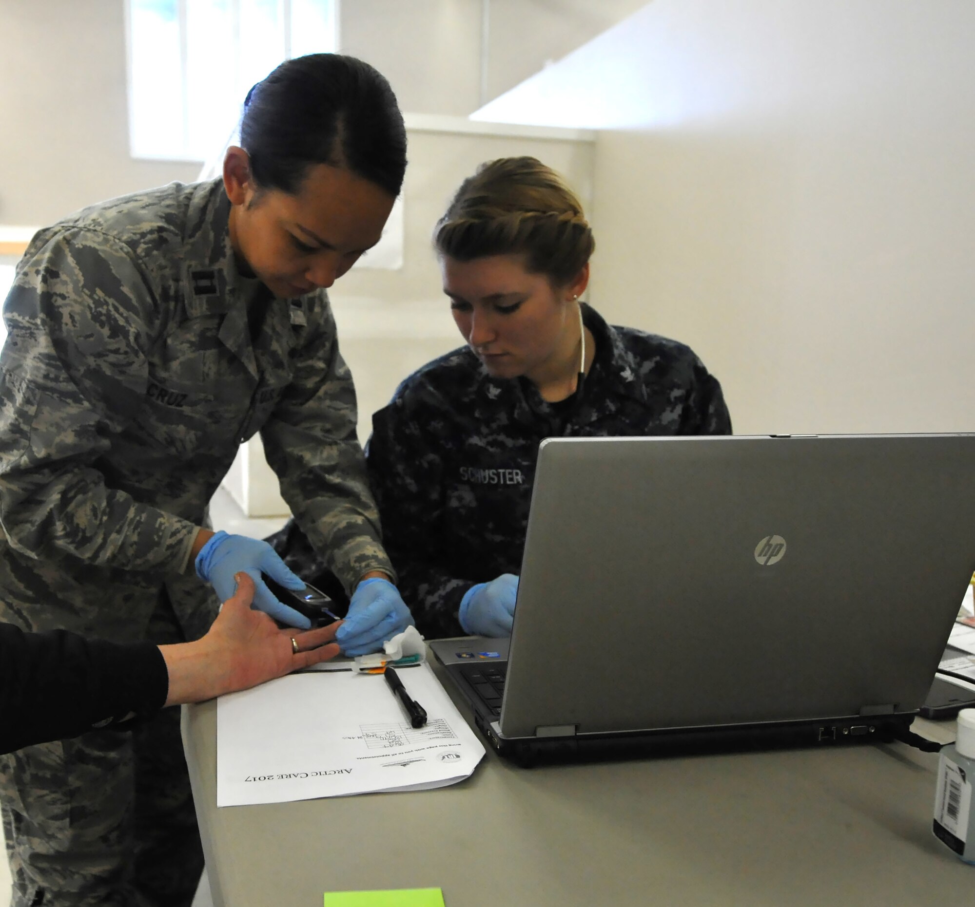 U.S. Air Force Capt. Anna Maria Cruz, a nurse assigned to the 624th Aerospace Medical Squadron and Navy Petty Officer Third Class Kiara Schuster work together on checking the blood sugar level of a patient during ARCTIC CARE 2017 medical readiness training exercise on March 28, 2017, Kodiak, Alaska. ARCTIC CARE provides service members an opportunity to simulate a forward deployed environment while serving the all the citizens of Kodiak, Alaska. (U.S. Air Force photo by Master Sgt. Luke Johnson)