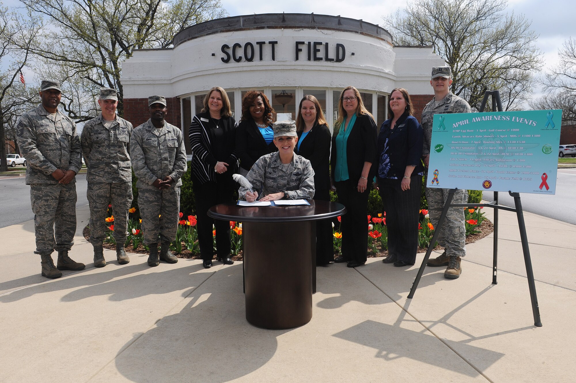 Col. Laura Lenderman, 375th Air Mobility Wing commander, signs an awareness proclamation April 4 in front of the historical gate. This year, the base is combining Sexual Assault Awareness Month, Green Dot, Alcohol and Drug Prevention and Treatment, Child Abuse Prevention, Autism Awareness, and Month of the Military Child under one unified effort to raise awareness about those campaigns. Back row: Chief Master Sgt. Wesley Mathias, 375th AMW command chief; Col. William Buschur, 375th AMW vice commander; Capt. Ed Jones, Alcohol and Drug Prevention and Treatment program manager; Shannon Dauber; Airman and Family Readiness airman and family services chief; Mauranda Bembry, 375th Medical Group Family Advocacy program manager; Jamie Mattice, 375th AMW Sexual Assault Program and Response specialist; Brenda Wells, 375th AMW primary prevention of violence specialist; Monica Stouffer, A&FRC chief; and Capt. Travis Hough, SAPR deputy sexual assault response coordinator.