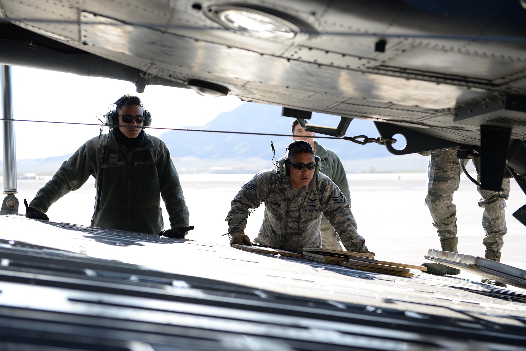 Airmen, 34th Weapons Squadron, check a winch cable before loading an HH-60 Pave Hawk helicopter onto a C-17 Globemaster III, assigned to the 57th Weapons Squadron, McChord Air Force Base, Wash., March 28, 2017, at Nellis Air Force Base, Nev. The C-17 Globemaster III cargo aircraft is capable of carrying personnel, vehicles and other aircraft over long distance travel. (U.S. Air Force photo by Airman 1st Class Andrew D. Sarver/ Released)