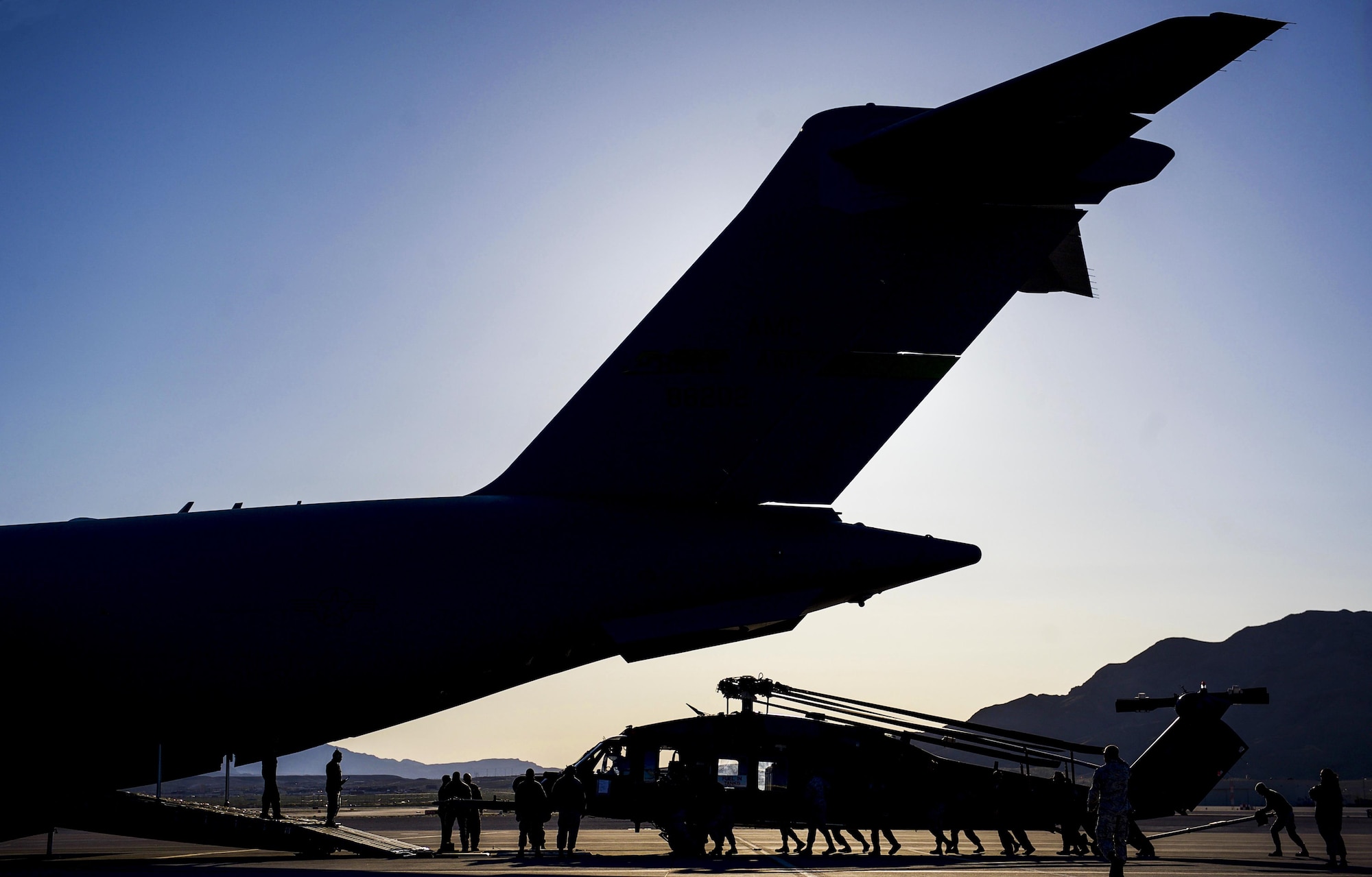 Airman push an HH-60 Pave Hawk assigned to the 34th Weapons Squadron, into position as it is loaded into a C-17 Globemaster III assigned to the 57th Weapons Squadron, McChord Air Force Base, Wash., March 28, 2017. The C-17 Globemaster has the load capacity to haul two HH-60 Pave Hawks. (U.S. Air Force photo by Airman 1st Class Kevin Tanenbaum/Released)