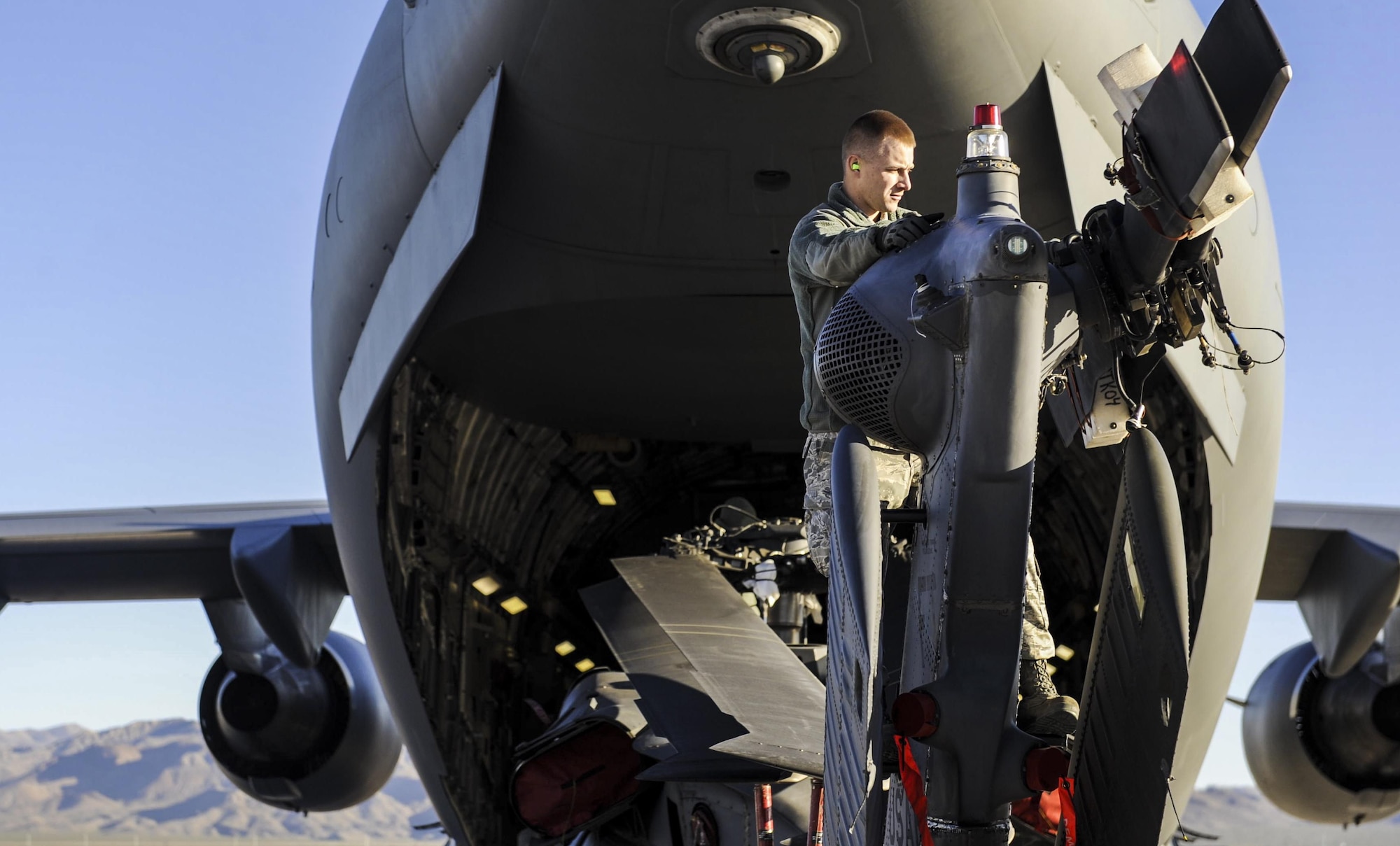 An Airman, 34th Weapons Squadron, aligns the rear rotor of an HH-60 Pave Hawk as it is loaded into a C-17 Globemaster III assigned to the 57th Weapons Squadron, McChord Air Force Base, Wash., before traveling to Fort Riley, Kan., March 28, 2017. Once landing at Fort Riley, part of the training consisted of how quickly the HH-60s could be unloaded from the C-17. (U.S. Air Force photo by Airman 1st Class Kevin Tanenbaum/Released) 