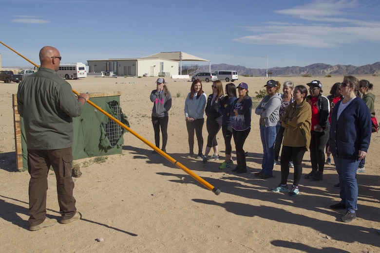 Dave Andrew, counter Improvised Explosive Device instructor, Marine Corps Engineer School, teaches ITX for Spouses participants how to use a Holley stick at Range 800 aboard Marine Corps Air Ground Combat Center, Twentynine Palms, Calif., March 30, 2017. The Holley stick is a tool used exclusively by Marine Corps explosive ordnance disposal technicians that provides them with the capability to investigate and manipulate a suspect IED from a stand-off distance.  (U.S. Marine Corps photo by Cpl. Connor Hancock)