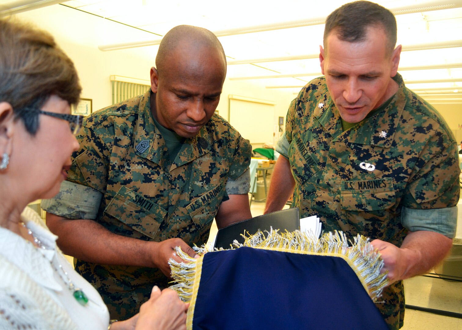 Marine Sgt. Maj. Gary Smith, Marine Corps Systems Command senior enlisted Marine, and Marine Lt. Col. Christopher Madeline, product manager for Reconnaissance and Amphibious Raids, inspect the threads of a flag in the DLA Troop Support flag room April 5, presented by Hue Nguyen, flag room supervisor.