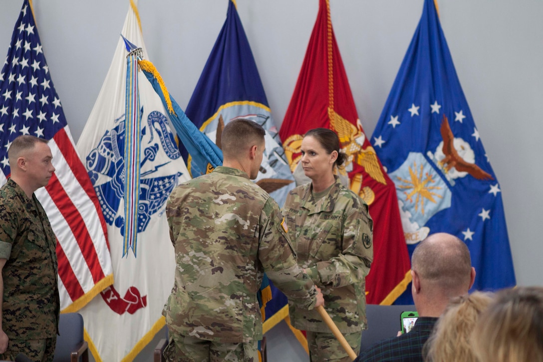 Army 1st Sgt. Janine Burr passes the organizational flag to DLA Distribution Susquehanna, Pennsylvania, commander Army Col. Brad Eungard, symbolizing her last act as the organization’s first female senior enlisted advisor as Marine Master Sgt. Bryan Alberts looks on.  