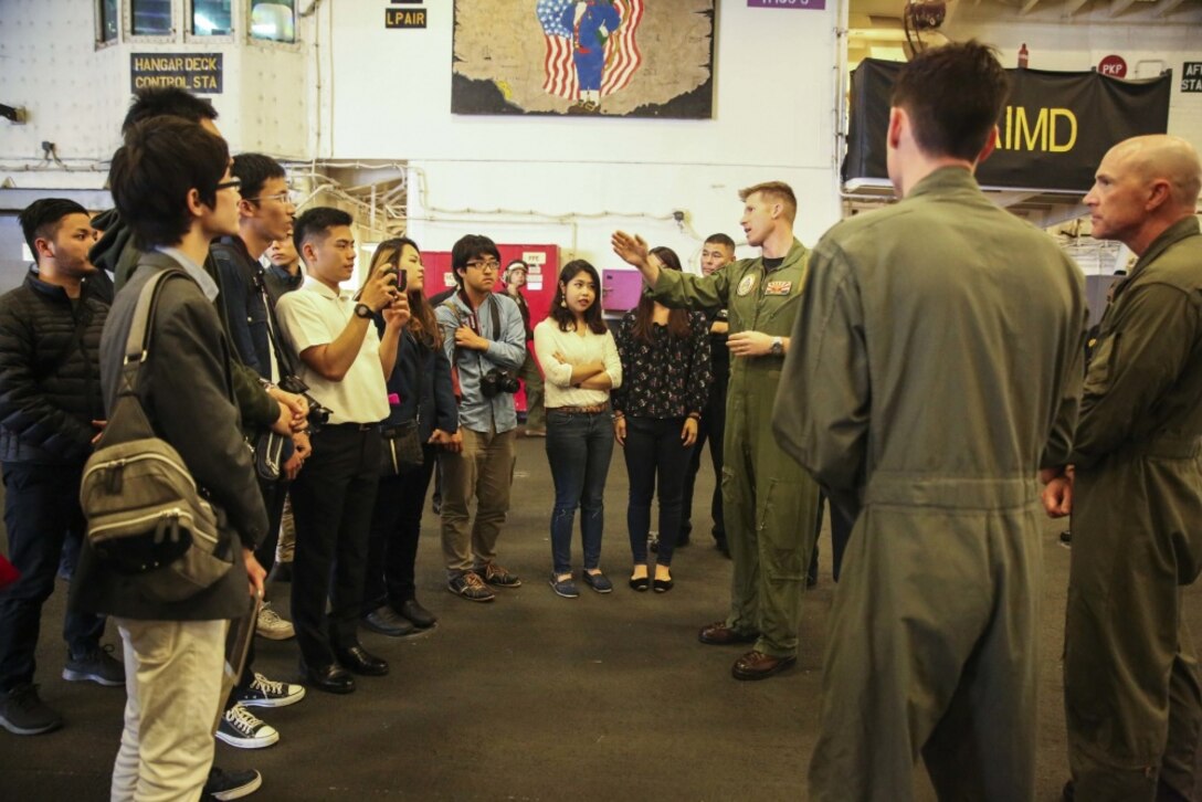 College students from Okinawa, Japan listen to a presentation from Navy pilot Lt. Cmdr. John Kadz in the hangar bay of the USS Bonhomme Richard (LHD 6), in the Pacific Ocean, March 25, 2017. College students from Okinawa International University, Ryukyu University and Toyo Medical Community College toured the USS Bonhomme Richard (LHD 6) as part of a military exchange experience during the 31st Marine Expeditionary Unit’s 17.1 Spring Patrol of the Indo-Asia-Pacific region. Education programs, such as this military exchange experience, increase cooperation, trust and understanding between the U.S. military and the Okinawan community. As the Marine Corps’ only continuously forward deployed unit, the 31st Marine Expeditionary Unit’s air-ground-logistics team provides a flexible force, ready to perform a wide range of military operations, from limited combat to humanitarian assistance operations, throughout the Asia-Pacific region. (U.S. Marine Corps photo by Sgt. Tiffany Edwards/Released)