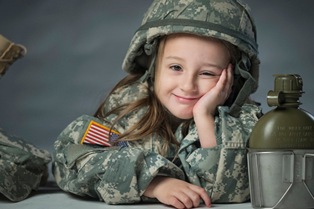 Army Sgt. James Newby's daughter Lily grins as she poses for portraits with her father's uniform items at Fort Meade, Md., March 18, 2015. Air Force photo by Staff Sgt. Vernon Young Jr.