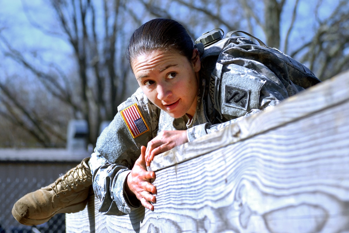 A soldier climbs over a high wall during a competition.