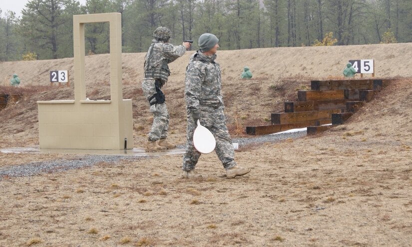 (Background) A competitor fires a 9mm pistol at the qualification course as a range safety officer (foreground) checks for safety issues at Fort Devens, Massachusetts, April 4, 2017, as part of the 2017 Joint 80th Training Command and 99th Regional Support Command Best Warrior Competition.