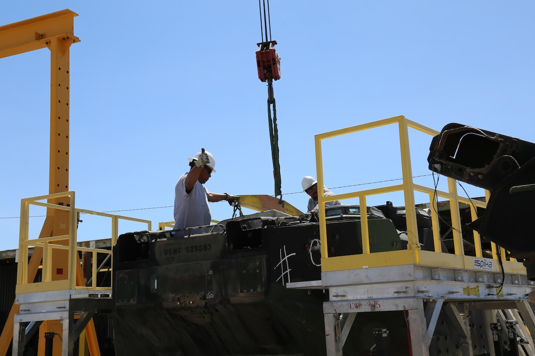 (Left) Daniel Espinoza and Fred Steens, riggers for Material Handling Equipment section, signal directions to the operator of a portable crane during the lifting of an engine from an Amphibious Assault Vehicle April 4. Riggers are responsible for safely attaching anything to be lifted to the device that is lifting it so that it is not overbalanced at Production Plant Barstow, Marine Depot Maintenance Command, aboard the Yermo Annex of Marine Corps Logistics Base Barstow, Calif.