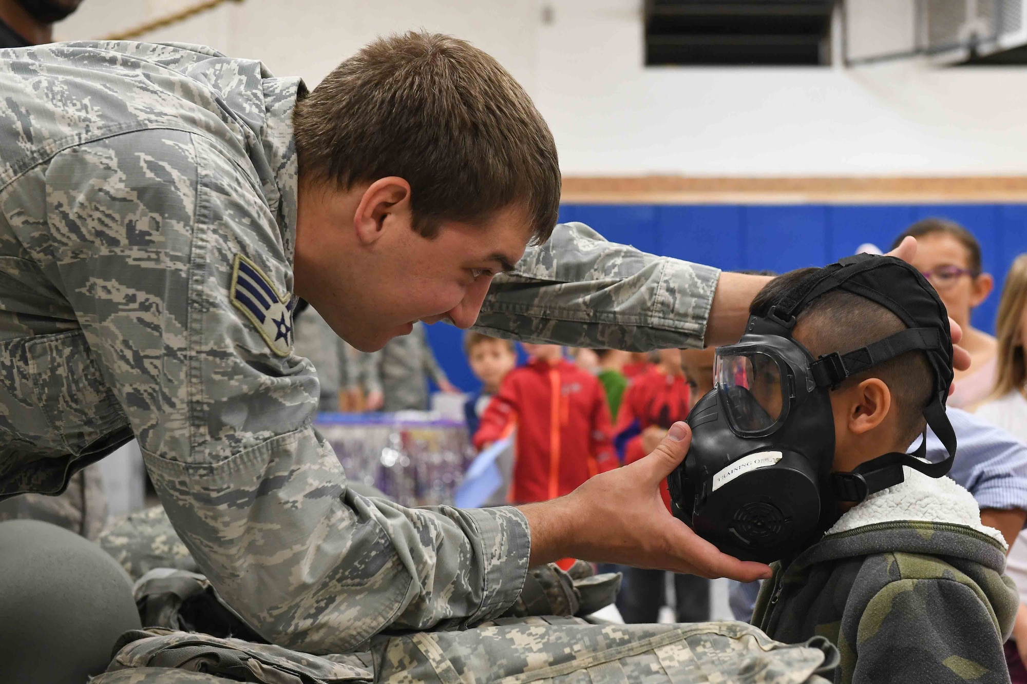 Senior Airman Jacob Peters, 75th Logistics Readiness Squadron, assists a student trying on a gas mask during the Kids Deployment Day event, Hill Field Elementary, Utah, April 14, 2017. (U.S. Air Force photo/R. Nial Bradshaw)