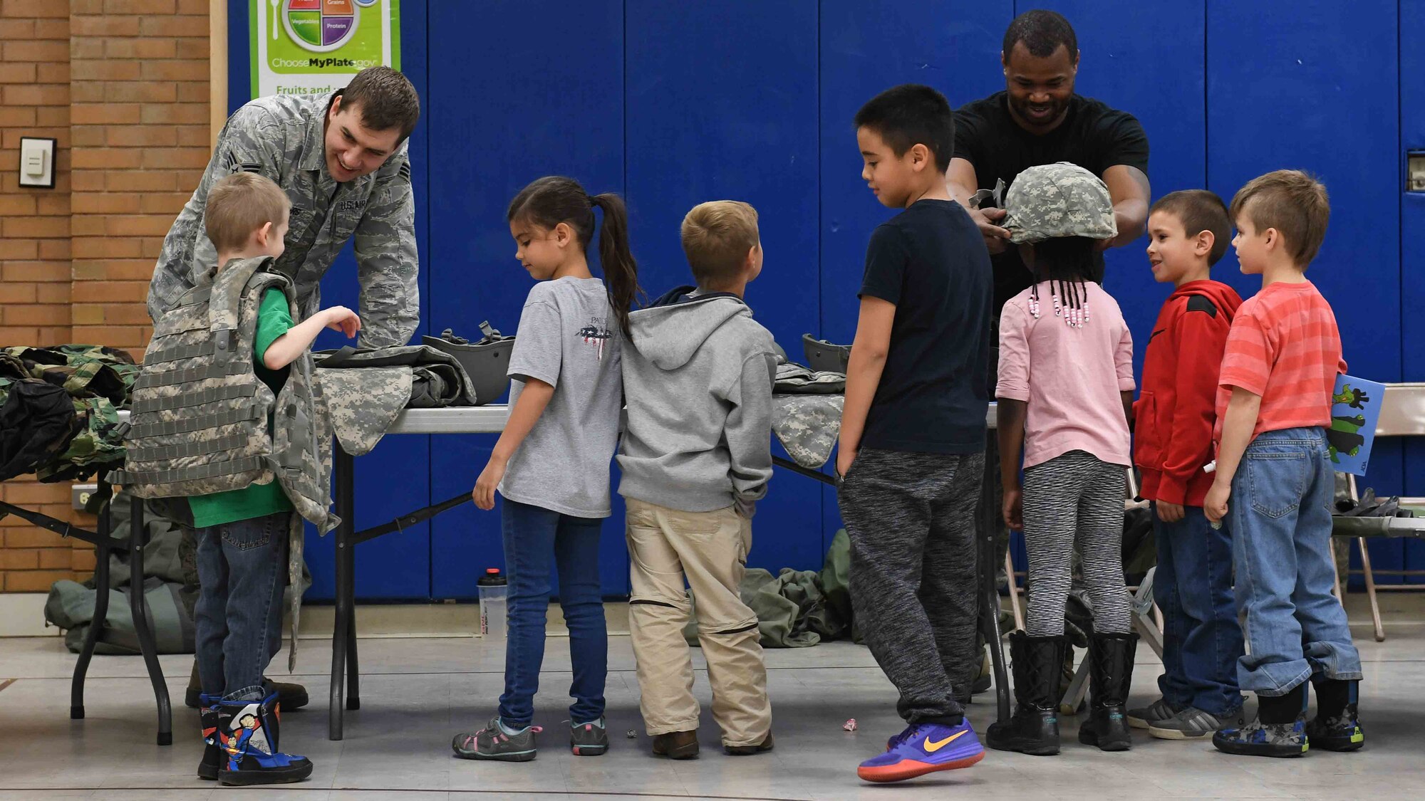 Senior Airman Jacob Peters and Staff Sgt. Deqoune Kennedy answer questions and assist students trying on military gear during the Kids Deployment Day event, Hill Field Elementary, Utah, April 14, 2017. (U.S. Air Force photo/R. Nial Bradshaw)