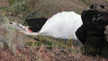 View of the "Rooster Tail", Lucky Peak Dam, May 25, 2008, Boise, Idaho. A popular springtime attraction is the "Rooster Tail" which results from the discharge of water through the original release structures of the dam under pressure from the lake above.  Using a "flip bucket" to direct the spray high into the air, the erosive, scouring force of the water is greatly dissipated as it rises, rests and slowly falls back to the stream channel.
The Rooster Tail only uses water from large releases required for flood risk management that exceed powerhouse capacity, thus no water is wasted for the display.   
It occurred daily until 1986 when construction of the Lucky Peak Power Plant Project started.  
