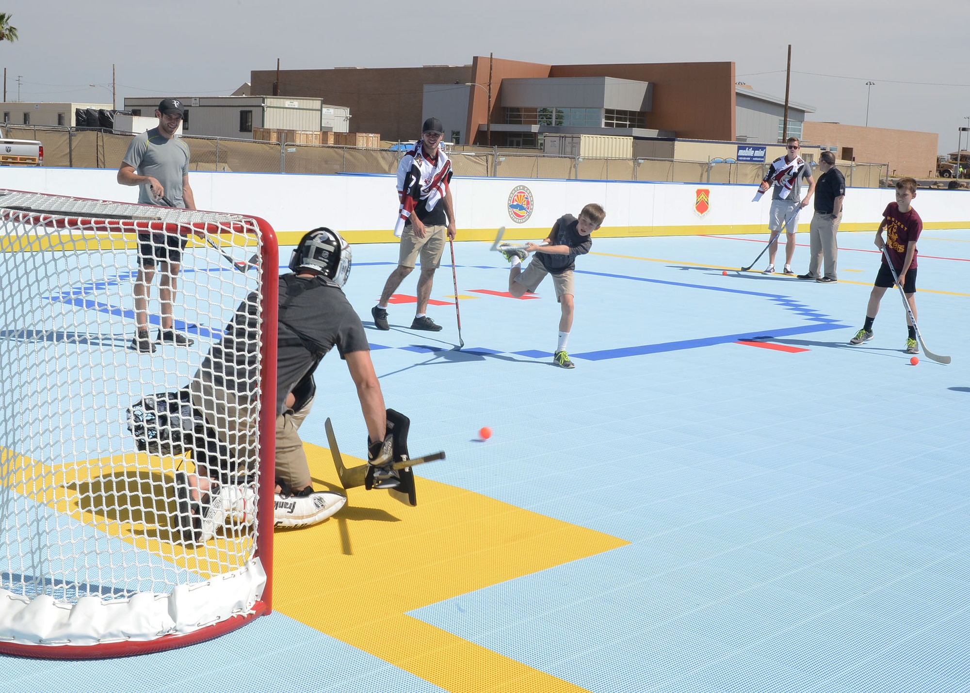 Luke family members take aim at Arizona Coyotes prior to the ribbon cutting ceremony for the new deck hockey rink April 13, 2017, at Luke Air Force Base, Ariz. Connor Murphy, Anthony DeAngelo, Alex Goligoski and Jordan Martinook from the Coyotes attended the ribbon cutting ceremony to show support and give Luke Airmen some hockey tips. (U.S. Air Force photo by Senior Airman James Hensley)