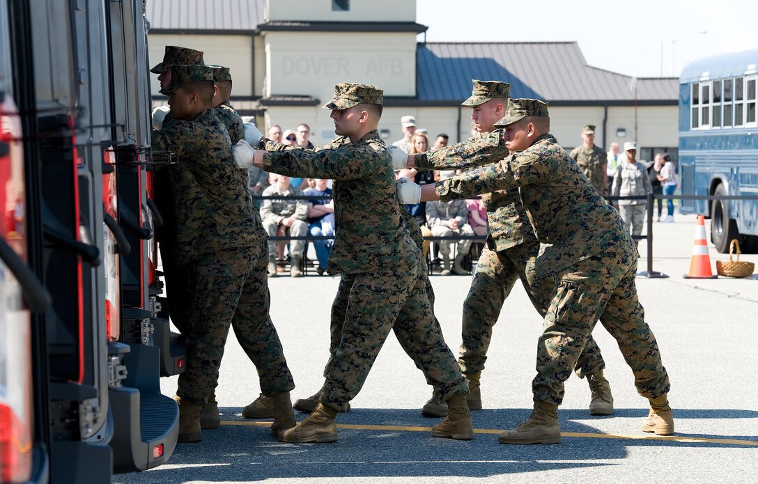 A U.S. Marine Corps carry team stands by after placing a transfer case in the mortuary transfer vehicle during a simulated dignified transfer April 11, 2017, on Dover Air Force Base, Del. In the background, individuals who played the role of family members attending the dignified transfer, watched the Marines carry the simulated fallen service member off the C-17 Globemaster III, past the official party and into the MTV. (U.S. Air Force photo by Roland Balik)