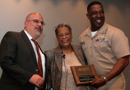 Naval Surface Warfare Center Dahlgren Division (NSWCDD) leaders present a plaque to Raye Montague in appreciation of her keynote speech at the command sponsored Women's History Month Observance. Montague was the first person to design a U.S. Navy ship - the USS Oliver Hazard Perry (FFG-7) - using a computer, revolutionizing naval ship design. The Navy's "hidden figure" spoke about her life and career experiences, sharing her words of wisdom to all gathered at the Naval Support Facility (base) theater to celebrate the observance. Standing left to right: NSWCDD Technical Director John Fiore; Montague; and NSWCDD Commanding Officer Capt. Godfrey 'Gus' Weekes. 