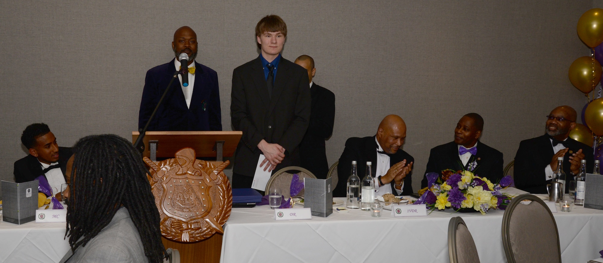 A RAF Lakenheath High School student, center, is awarded an $800 scholarship April 18, 2017, for his submission to an essay contest awarded by the Omega Psi Phi Fraternity Inc., at a banquet in Birmingham, England. Sitting at the head table were district representatives and leaders of the fraternity. The evening was held to celebrate the fifth anniversary of the Chi Mu Mu chapter in the U.K. (U.S. Air Force photo by Senior Airman Justine Rho)