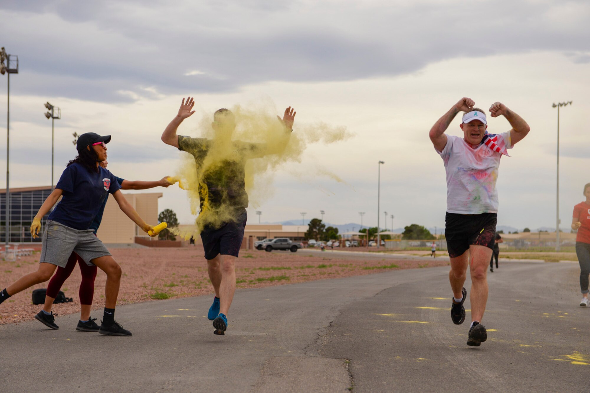 Staff Sgt. Dominique Lindsey, 99th Medical Operations Squadron mental health technician, tosses yellow powder on an Airman while Col. Paul Murray, the 99th Air Base Wing commander, runs through the checkpoint unscathed at the 5k Color Run/Walk, April 7, 2017, at Nellis Air Force Base, Nev. Volunteers from base agencies around Nellis set up stations for Airmen to run through and get covered with colored powder. (U.S. Air Force photo by Airman 1st Class Andrew D. Sarver/ Released)

