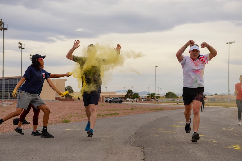 Staff Sgt. Dominique Lindsey, 99th Medical Operations Squadron mental health technician, tosses yellow powder on an Airman while Col. Paul Murray, the 99th Air Base Wing commander, runs through the checkpoint unscathed at the 5k Color Run/Walk, April 7, 2017, at Nellis Air Force Base, Nev. Volunteers from base agencies around Nellis set up stations for Airmen to run through and get covered with colored powder. (U.S. Air Force photo by Airman 1st Class Andrew D. Sarver/ Released)

