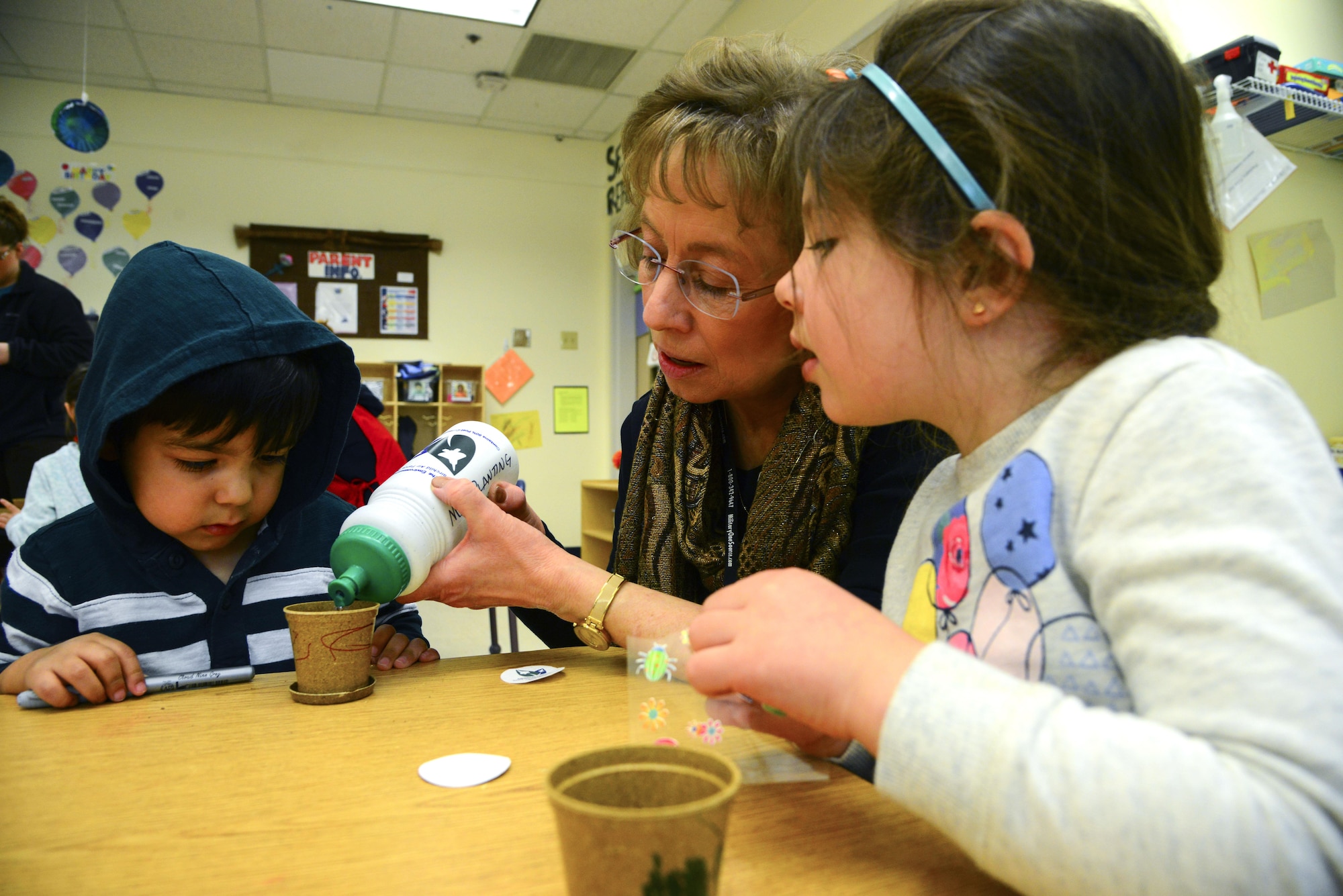 Kids from the Child Development Center observe as Diane Wulf, 92nd Civil Engineer Squadron pollution prevention program manager, pours water into a mini planter during the Earth Day celebration Apr. 20, 2017, at Fairchild Air Force Base, Washington. Airmen observed the day by reading stories relating to Earth Day to children and had them plant their own seeds in a mini planter. (U.S. Air Force photo/Senior Airman Janelle Patiño)