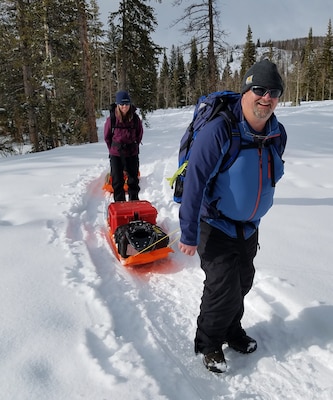 CRREL Researchers Dr. Carrie Vuyovich (back) and Art Gelvin (front) use sleds to transport the terrestrial laser scanner from the Local-Scale Observation Site. Scans were completed in snow-on and snow-off conditions to determine snow distribution and relate that to other instruments.