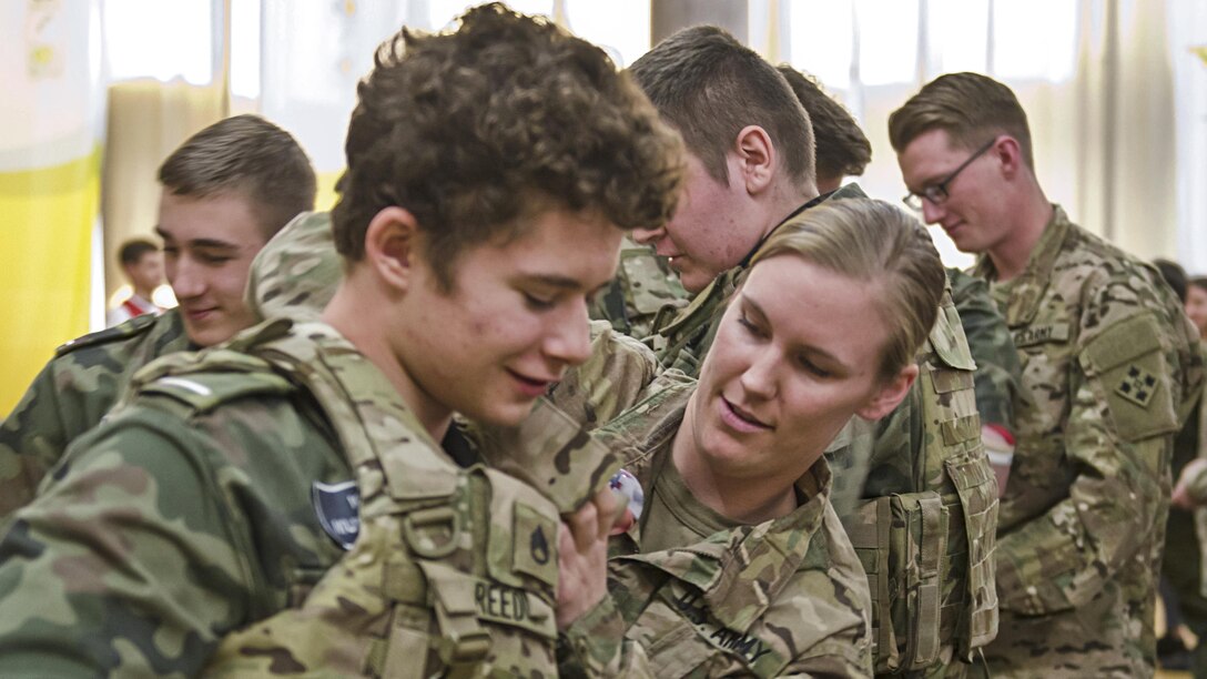 Army Staff Sgt. Kacie Reed shows a student how to connect the shoulder latches on a tactical vest at a school career fair in Zielona Gora, Poland, April 20, 2017. Reed is a medical platoon sergeant with the 3rd Battalion, 29th Field Artillery Regiment. Army photo by Sgt. Justin Geiger